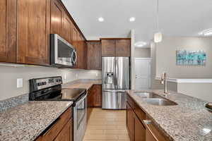 Kitchen with appliances with stainless steel finishes, hanging light fixtures, light stone counters, a textured ceiling, and light wood-style floors