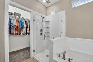 Full bathroom with a walk in closet, a shower stall, light colored carpet, and a garden tub