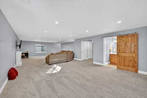 Living area featuring light colored carpet, a barn door, and recessed lighting