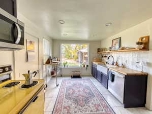 Kitchen with appliances with stainless steel finishes, open shelves, decorative backsplash, wooden counters, and light tile patterned flooring