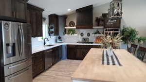 Kitchen with stainless steel appliances, dark brown cabinets, open shelves, decorative backsplash, and vaulted ceiling