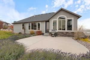 Back of house featuring a patio, stucco siding, roof with shingles, and stone siding