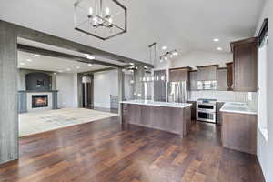 Kitchen featuring backsplash, open floor plan, a glass covered fireplace, appliances with stainless steel finishes, and hanging light fixtures