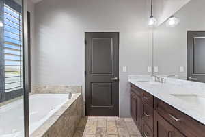 Full bathroom featuring a bath, double vanity, and stone tile floors