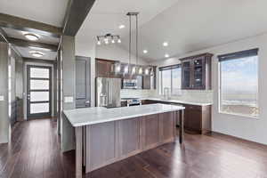 Kitchen featuring glass insert cabinets, stainless steel appliances, hanging light fixtures, lofted ceiling, and a center island