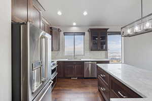Kitchen featuring stainless steel appliances, glass insert cabinets, dark brown cabinetry, and recessed lighting