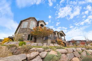 View of front of property featuring stone siding, a balcony, and stucco siding