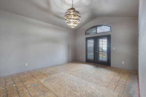 Empty room featuring lofted ceiling, french doors, and a chandelier