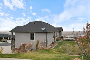 View of side of home featuring stucco siding, a lawn, and a shingled roof