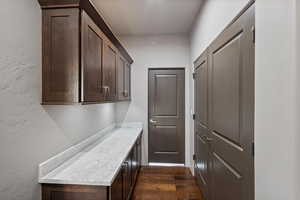 Laundry area with a textured wall and dark wood-type flooring