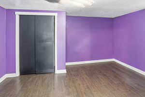 Unfurnished bedroom featuring a textured ceiling, dark wood-style floors, and a closet