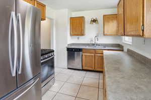 Kitchen featuring appliances with stainless steel finishes, brown cabinets, light tile patterned flooring, and light countertops