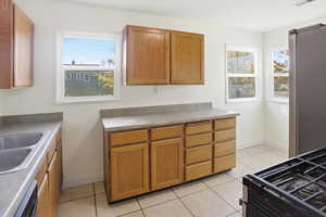 Kitchen with appliances with stainless steel finishes, light tile patterned floors, plenty of natural light, and brown cabinets