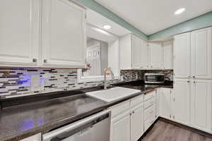 Kitchen with white cabinetry, stainless steel appliances, dark countertops, tasteful backsplash, and light wood-type flooring