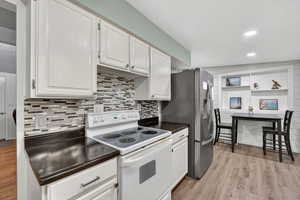 Kitchen featuring electric range, dark countertops, white cabinets, light wood-type flooring, and recessed lighting