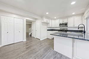 Kitchen featuring white cabinetry, a peninsula, dark stone counters, stainless steel appliances, and recessed lighting