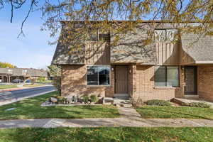View of front of home with brick siding, a front lawn, and roof with shingles
