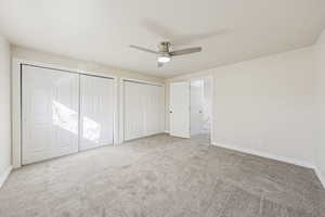 Unfurnished bedroom featuring carpet floors, multiple closets, and a ceiling fan