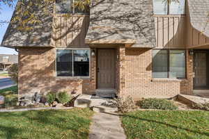 View of exterior entry with brick siding, roof with shingles, and a lawn
