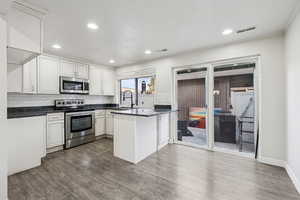 Kitchen with appliances with stainless steel finishes, backsplash, a peninsula, white cabinetry, and recessed lighting