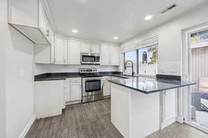 Kitchen featuring dark stone countertops, a peninsula, tasteful backsplash, stainless steel appliances, and recessed lighting