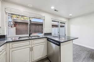 Kitchen with dark stone countertops, stainless steel dishwasher, dark wood finished floors, recessed lighting, and a peninsula