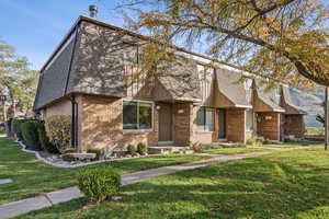 View of front facade with a front yard, brick siding, and roof with shingles
