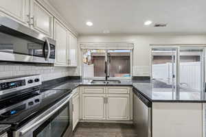 Kitchen featuring stainless steel appliances, a peninsula, dark stone countertops, tasteful backsplash, and recessed lighting