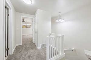 Hall featuring an upstairs landing, light carpet, and a chandelier