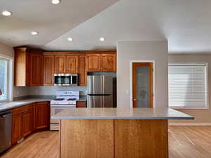 Kitchen featuring appliances with stainless steel finishes, a center island, brown cabinetry, recessed lighting, and light wood finished floors