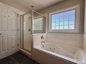 Bathroom featuring a tub with jets, a stall shower, and dark tile patterned floors