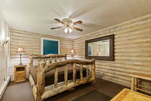 Bedroom featuring a textured ceiling, a baseboard heating unit, a ceiling fan, and rustic walls