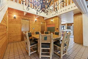 Dining space featuring wooden walls, light tile patterned floors, and a high ceiling