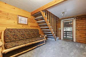 Living area with stairway, wooden walls, carpet flooring, a textured ceiling, and log walls
