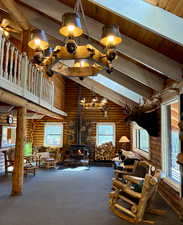Carpeted living room featuring high vaulted ceiling, a wood stove, and a wooden ceiling with exposed beams
