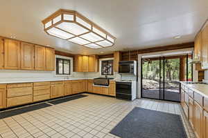 Kitchen with light countertops, electric range, light tile patterned floors, black microwave, and under cabinet range hood