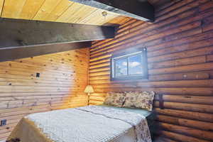 Bedroom featuring rustic walls and a wood ceiling with exposed beams