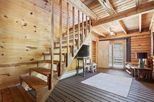 Stairs featuring hardwood / wood-style floors, rustic walls, and a wooden ceiling with exposed beams