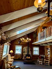Sitting room with a wood stove, a skylight, carpet flooring, a wooden ceiling with exposed beams, and high vaulted ceiling