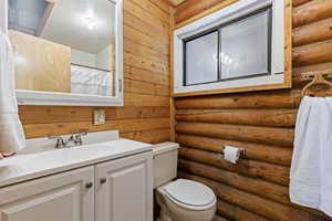 Full bathroom with log walls, a shower with curtain, and vanity