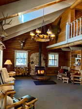 Carpeted living area with high vaulted ceiling, a wood stove, plenty of natural light, and a wood ceiling with exposed beams