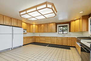 Kitchen with white appliances, light countertops, light tile patterned flooring, brown cabinetry, and recessed lighting