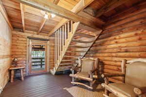 Unfurnished room with hardwood / wood-style flooring, a wood ceiling with exposed beams, stairway, and rustic walls
