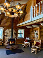 Living area with high vaulted ceiling, a wood stove, rustic walls, carpet flooring, and wood ceiling