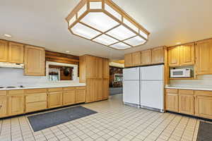 Kitchen featuring light countertops, white appliances, recessed lighting, light tile patterned floors, and under cabinet range hood