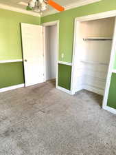 Unfurnished bedroom with ornamental molding, carpet, a ceiling fan, and a closet