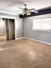 Unfurnished bedroom with carpet floors, a textured ceiling, a closet, a ceiling fan, and crown molding