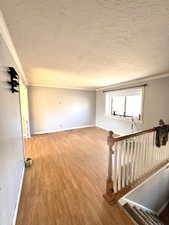 Unfurnished room featuring a textured ceiling, crown molding, and wood finished floors