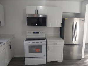 Kitchen featuring stainless steel appliances, white cabinetry, dark wood-type flooring, and light stone counters