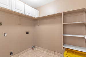 Laundry room featuring light tile patterned floors, cabinet space, and electric dryer hookup